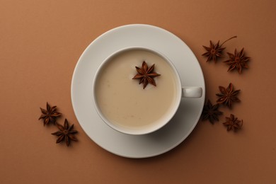 Photo of Cup of tea with milk and anise stars on brown background, flat lay