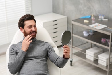 Man looking at his new dental implants in mirror indoors