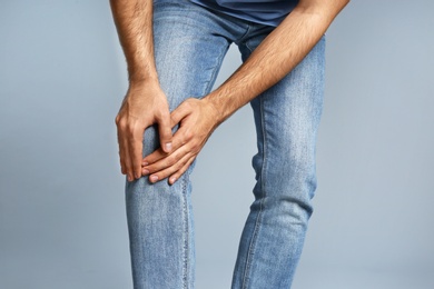 Man suffering from knee pain on grey background, closeup