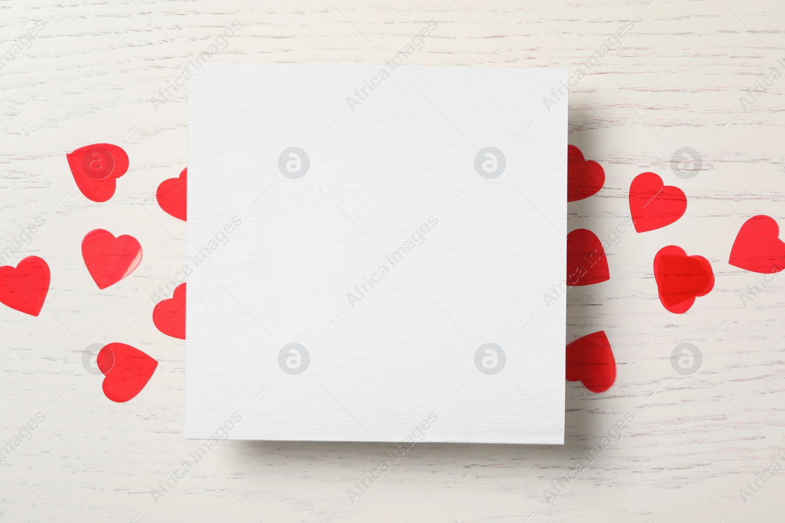 Photo of Blank card and red hearts on white wooden background, flat lay with space for text. Valentine's Day celebration