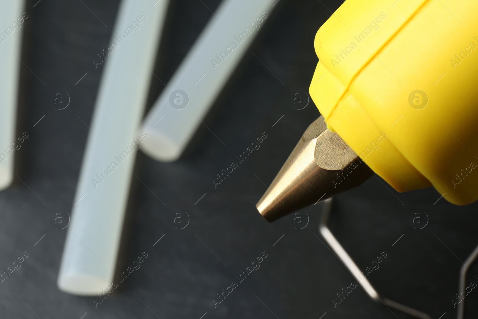 Photo of Hot glue gun and sticks on dark grey table, closeup