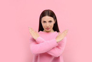 Photo of Stop gesture. Woman with crossed hands on pink background
