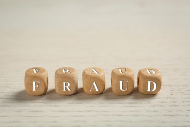 Photo of Word Fraud of cubes with letters on white wooden background. Space for text