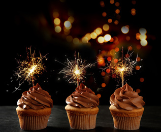 Image of Birthday cupcakes with sparklers on table against dark background