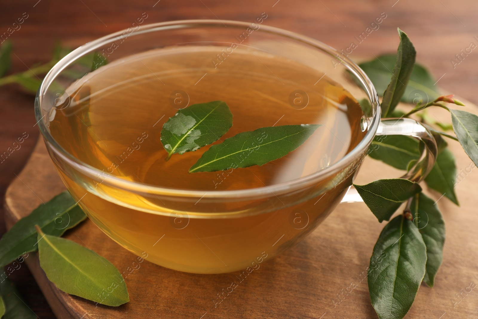 Photo of Cup of freshly brewed tea with bay leaves on wooden table, closeup