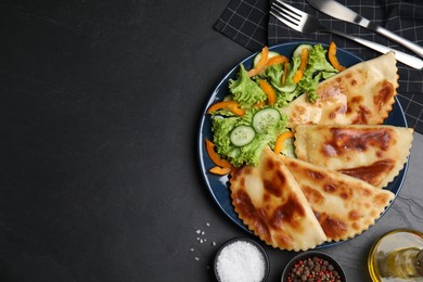 Photo of Delicious fried chebureki with vegetables served on black table, flat lay. Space for text