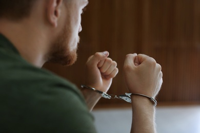 Man detained in handcuffs indoors, closeup view. Criminal law