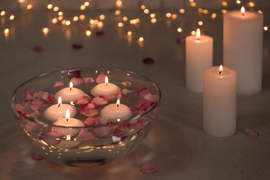Glass bowl with burning candles and petals on grey stone table