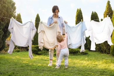 Mother and daughter hanging clothes with clothespins on washing line for drying in backyard