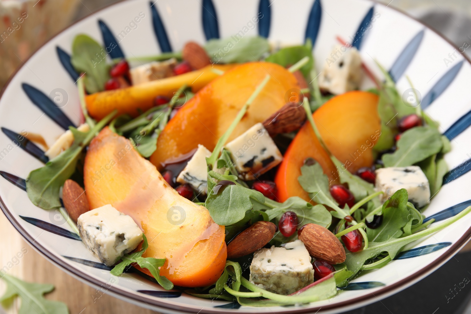 Photo of Tasty salad with persimmon, blue cheese, pomegranate and almonds served on table, closeup