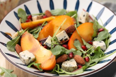 Tasty salad with persimmon, blue cheese, pomegranate and almonds served on table, closeup