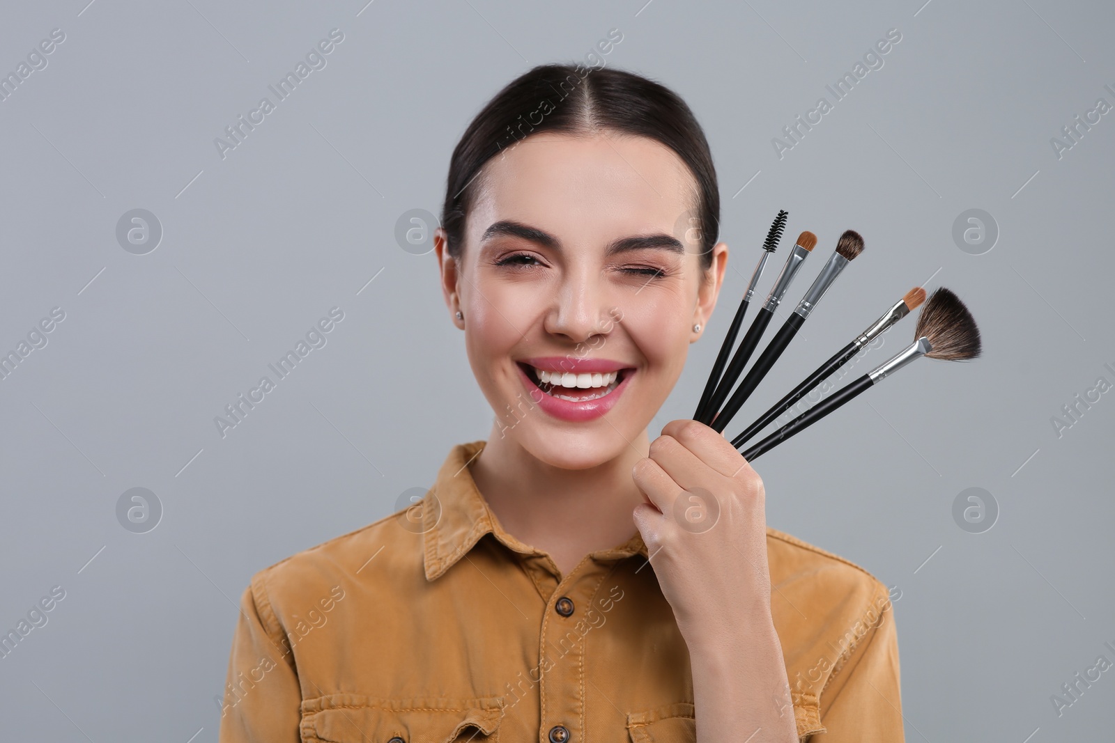 Photo of Happy woman with different makeup brushes on light grey background