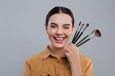 Photo of Happy woman with different makeup brushes on light grey background