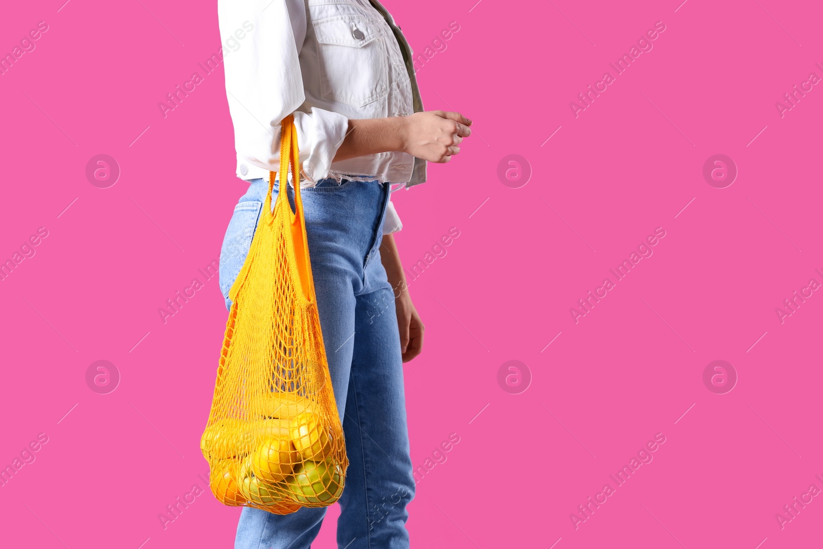 Photo of Woman holding net bag with fruits on pink background, closeup. Space for text