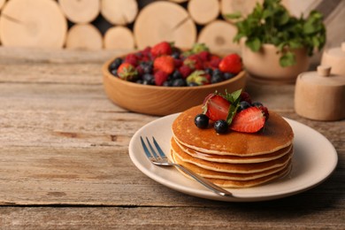 Photo of Stack of tasty pancakes with fresh berries and mint on wooden table. Space for text