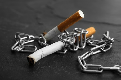 Photo of Cigarette stubs and chain on black table, closeup. Quitting smoking concept