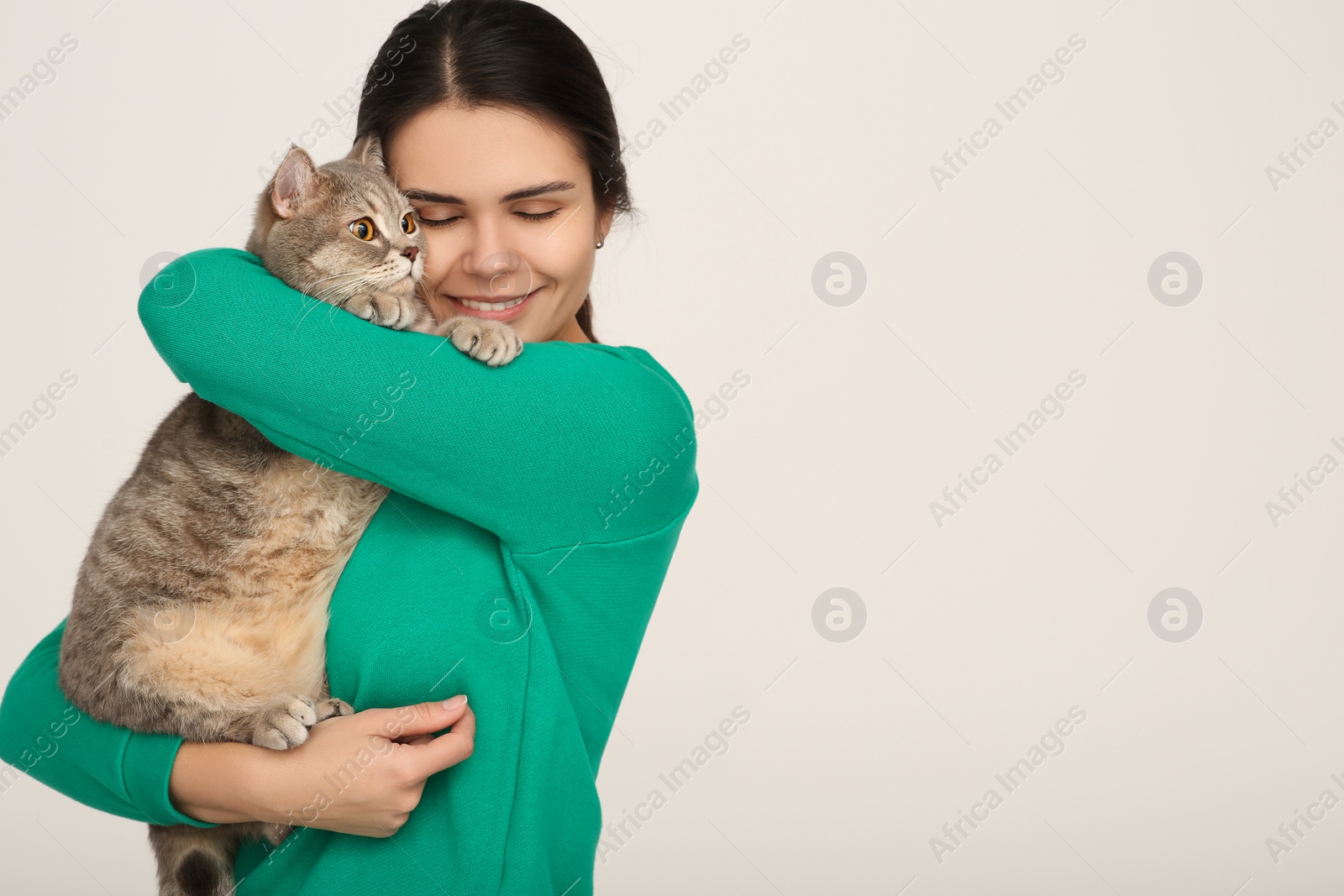 Photo of Young woman with adorable cat on light background, space for text