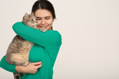 Young woman with adorable cat on light background, space for text