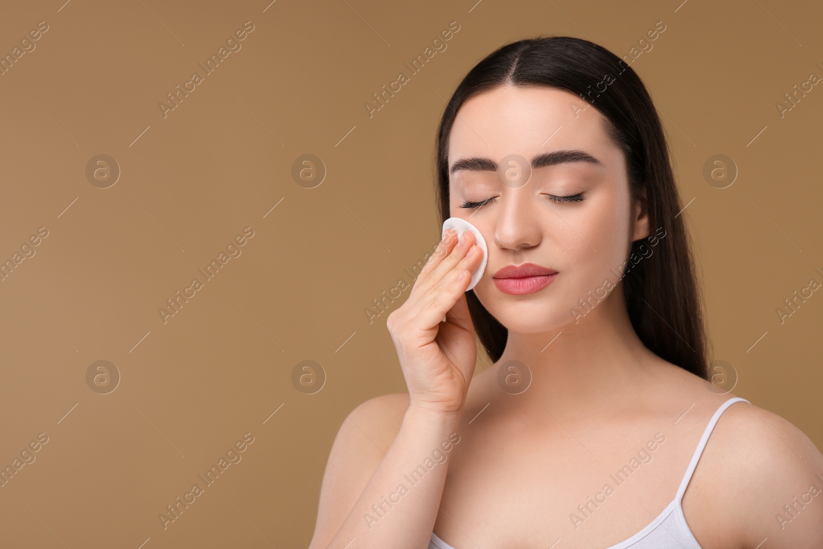 Photo of Beautiful woman removing makeup with cotton pad on beige background, space for text