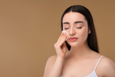 Beautiful woman removing makeup with cotton pad on beige background, space for text