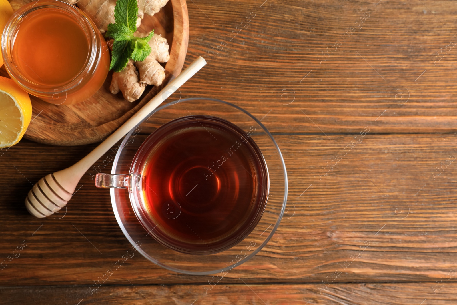 Photo of Cup of delicious ginger tea, honey and lemons on wooden table, flat lay. Space for text