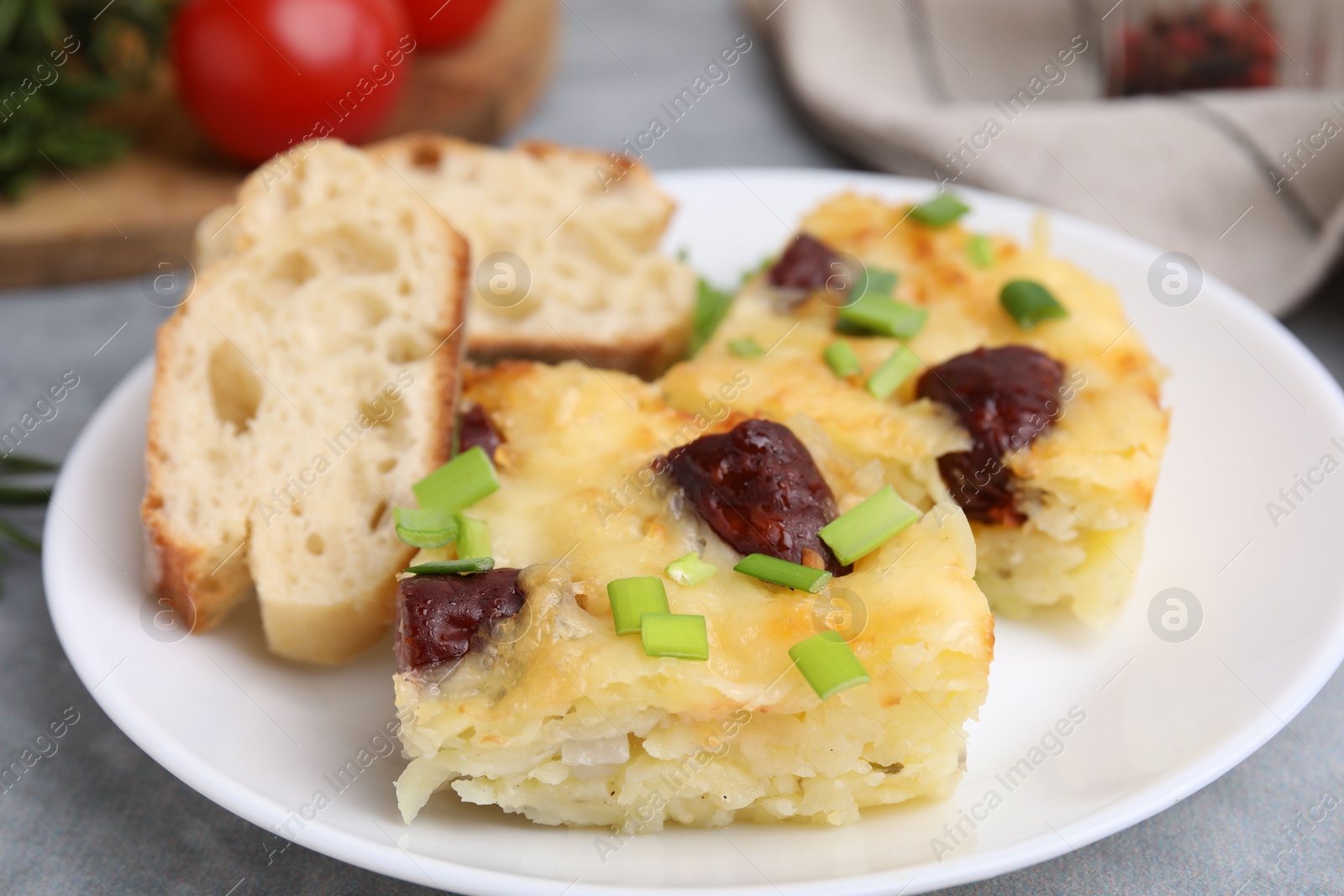 Photo of Tasty sausage casserole with green onion and bread on grey table, closeup