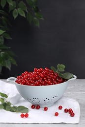 Photo of Ripe red currants and leaves in colander on grey textured table. Space for text