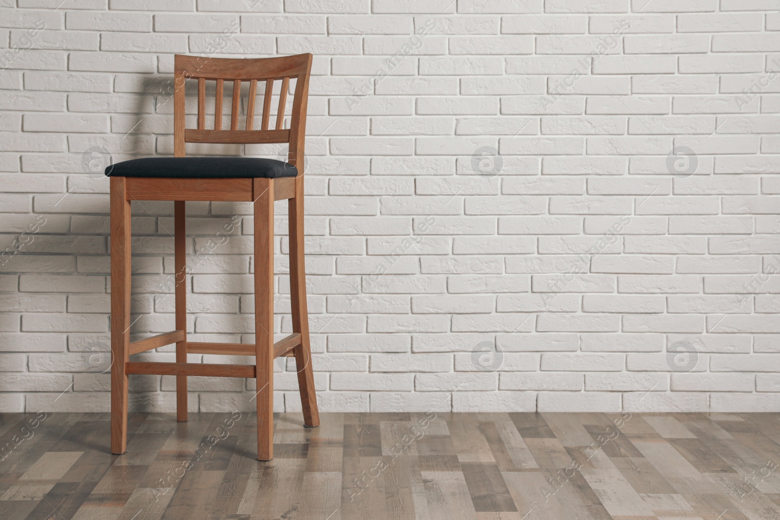 Photo of Stylish bar stool near white brick wall indoors. Space for text