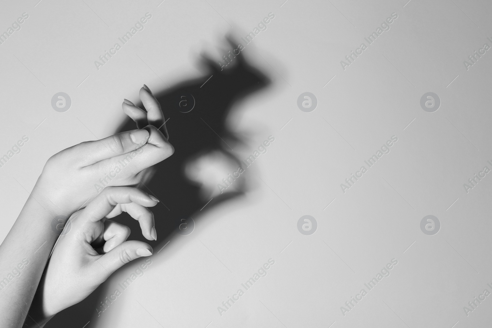 Photo of Shadow puppet. Woman making hand gesture like rabbit on light background, closeup with space for text. Black and white effect