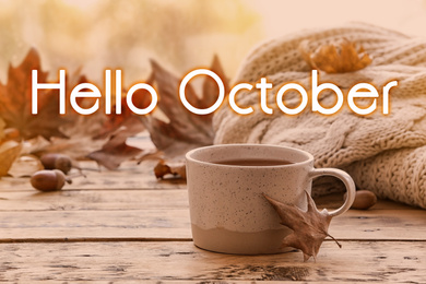 Image of Hello October card. Cup of hot drink and autumn leaves on wooden table