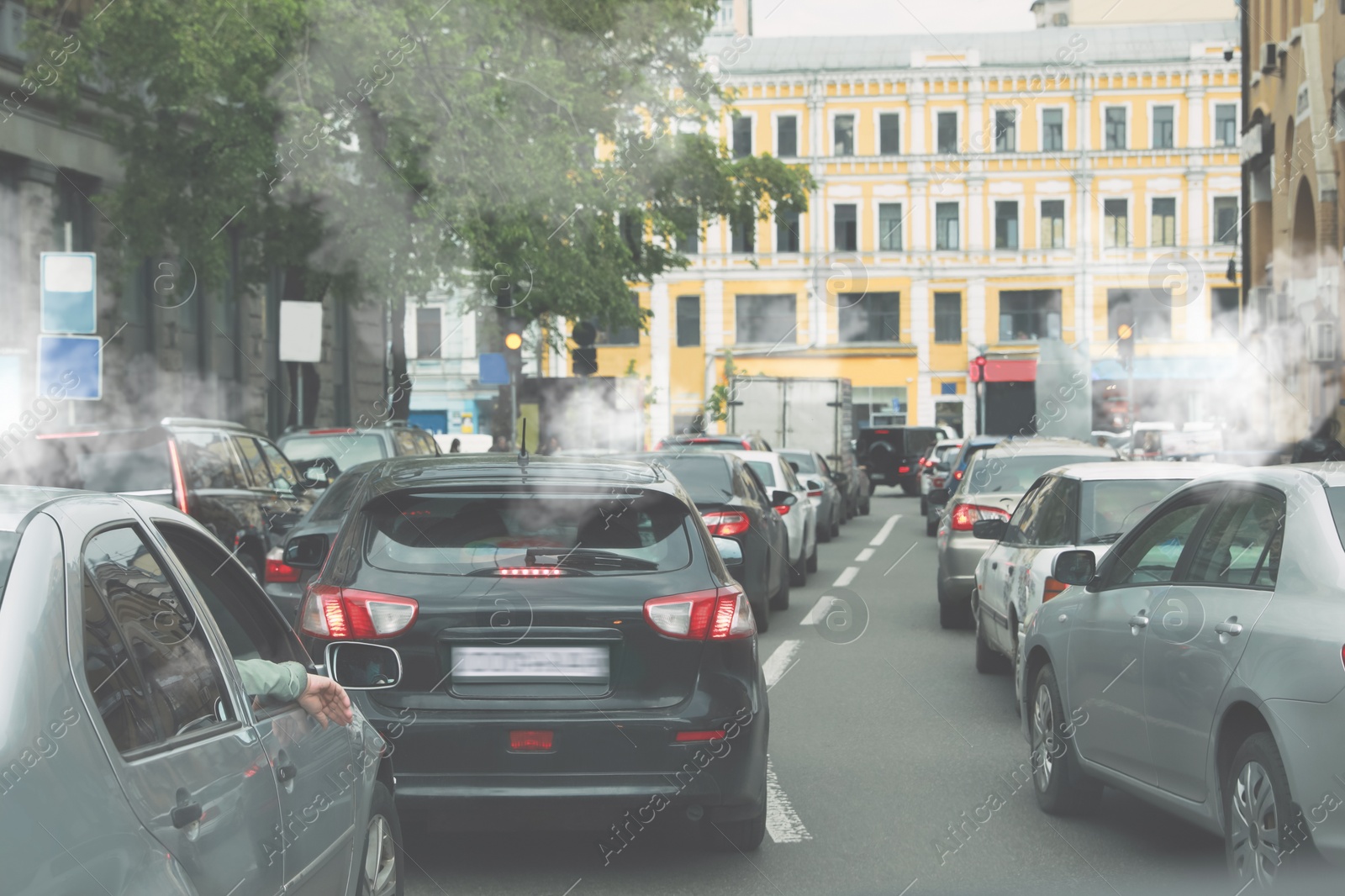 Image of Environmental pollution. Air contaminated with fumes in city. Cars surrounded by exhaust on road