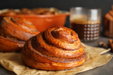 Photo of Parchment with freshly baked cinnamon roll on table, closeup