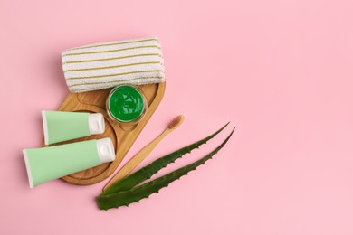 Photo of Tubes of toothpaste, fresh aloe, toothbrush and towel on pink background, flat lay. Space for text