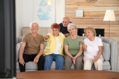 Happy elderly people watching TV together in living room