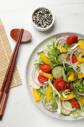 Tasty fresh vegetarian salad and chopsticks on white marble table, top view