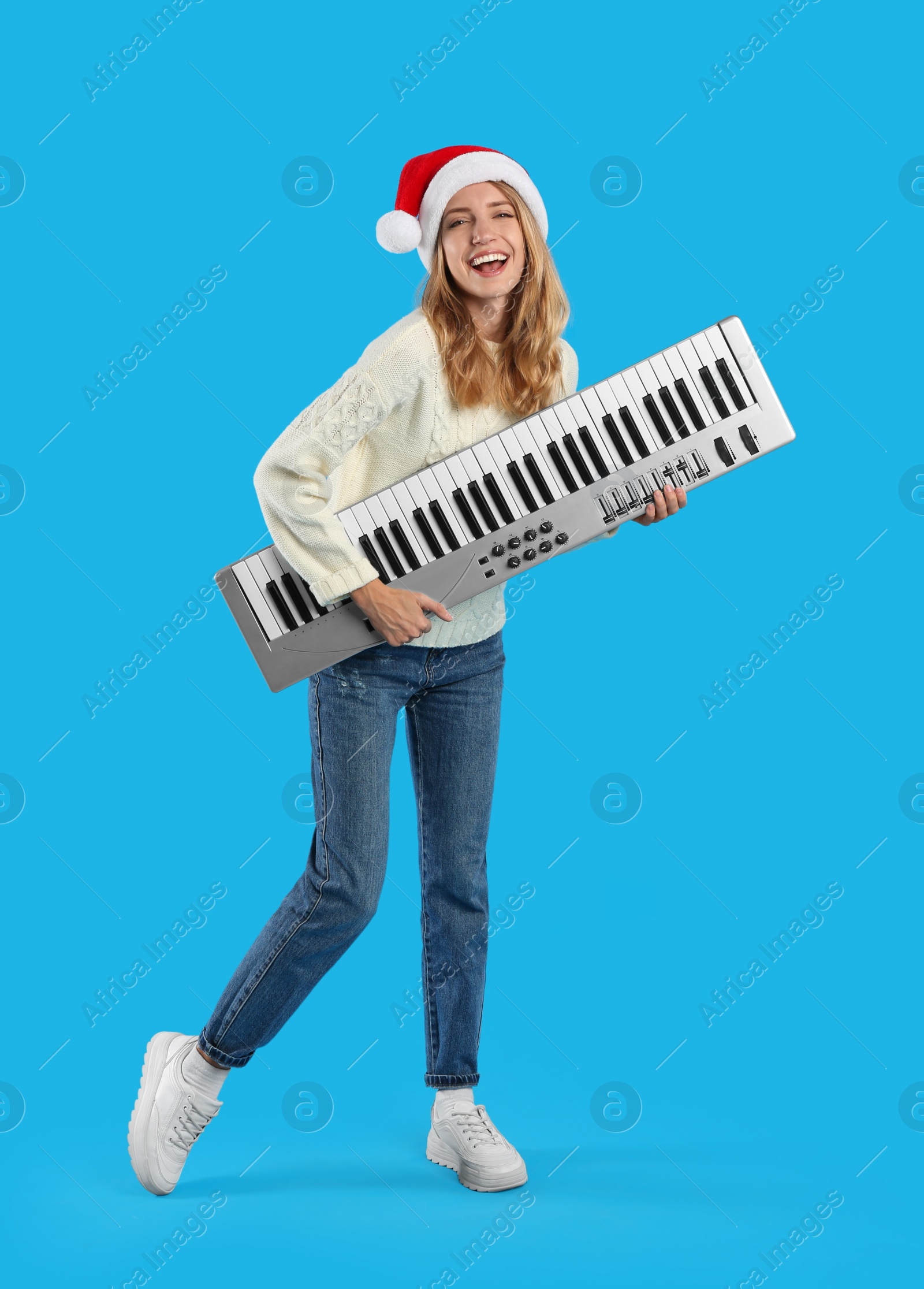 Photo of Young woman in Santa hat with synthesizer on light blue background. Christmas music