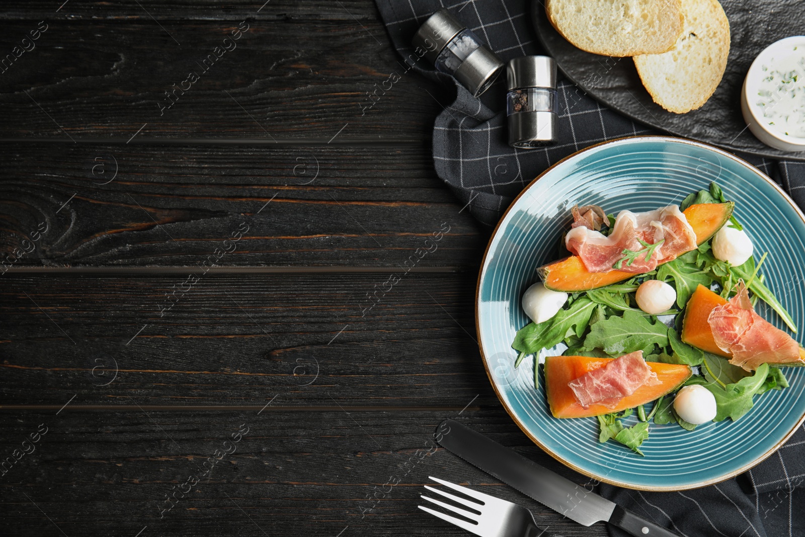 Photo of Flat lay composition of fresh melon with prosciutto on black wooden table. Space for text