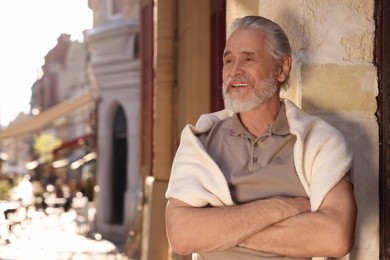 Handsome senior man standing near building outdoors, space for text