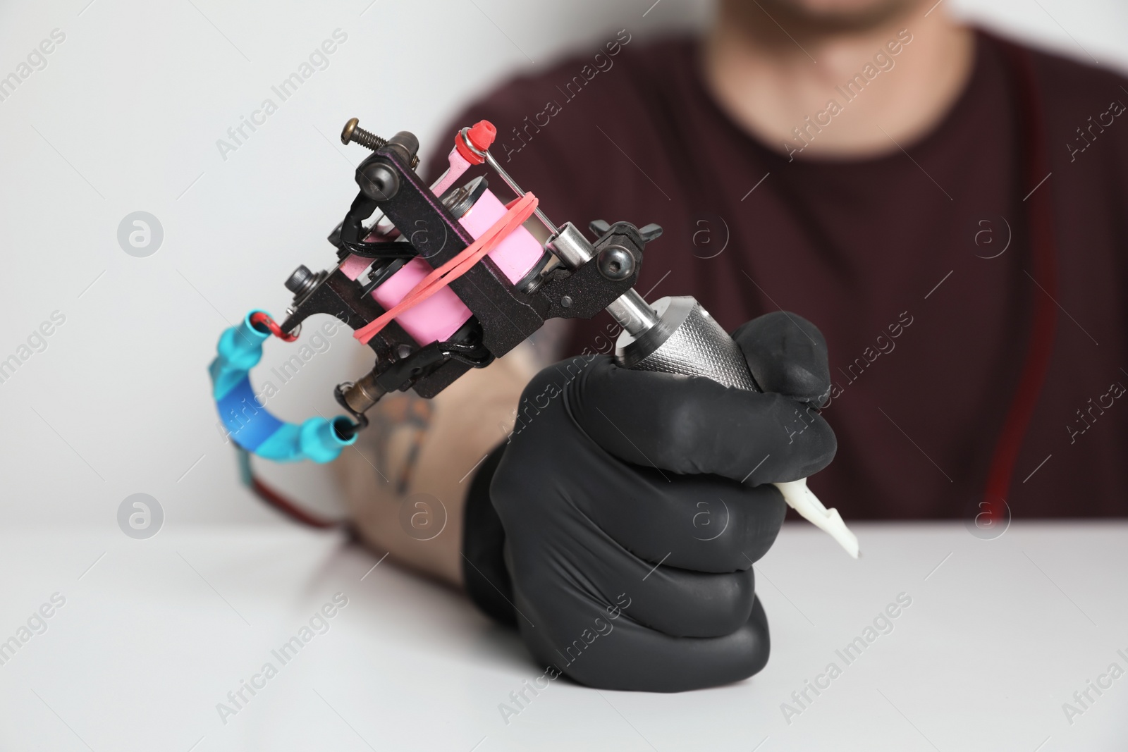 Photo of Tattoo artist with professional machine at table against light background, closeup