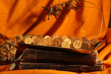 Wooden runes, dried plants and old books on orange fabric