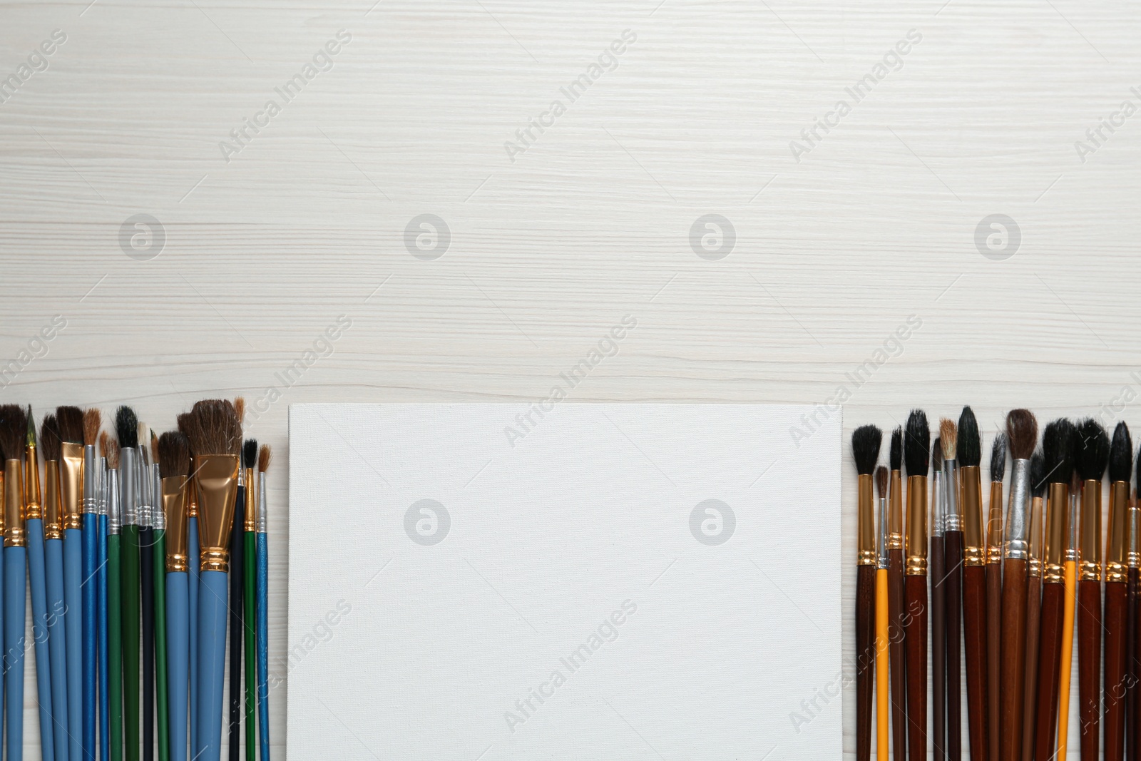 Photo of Blank canvas and brushes on white wooden table, flat lay. Space for text