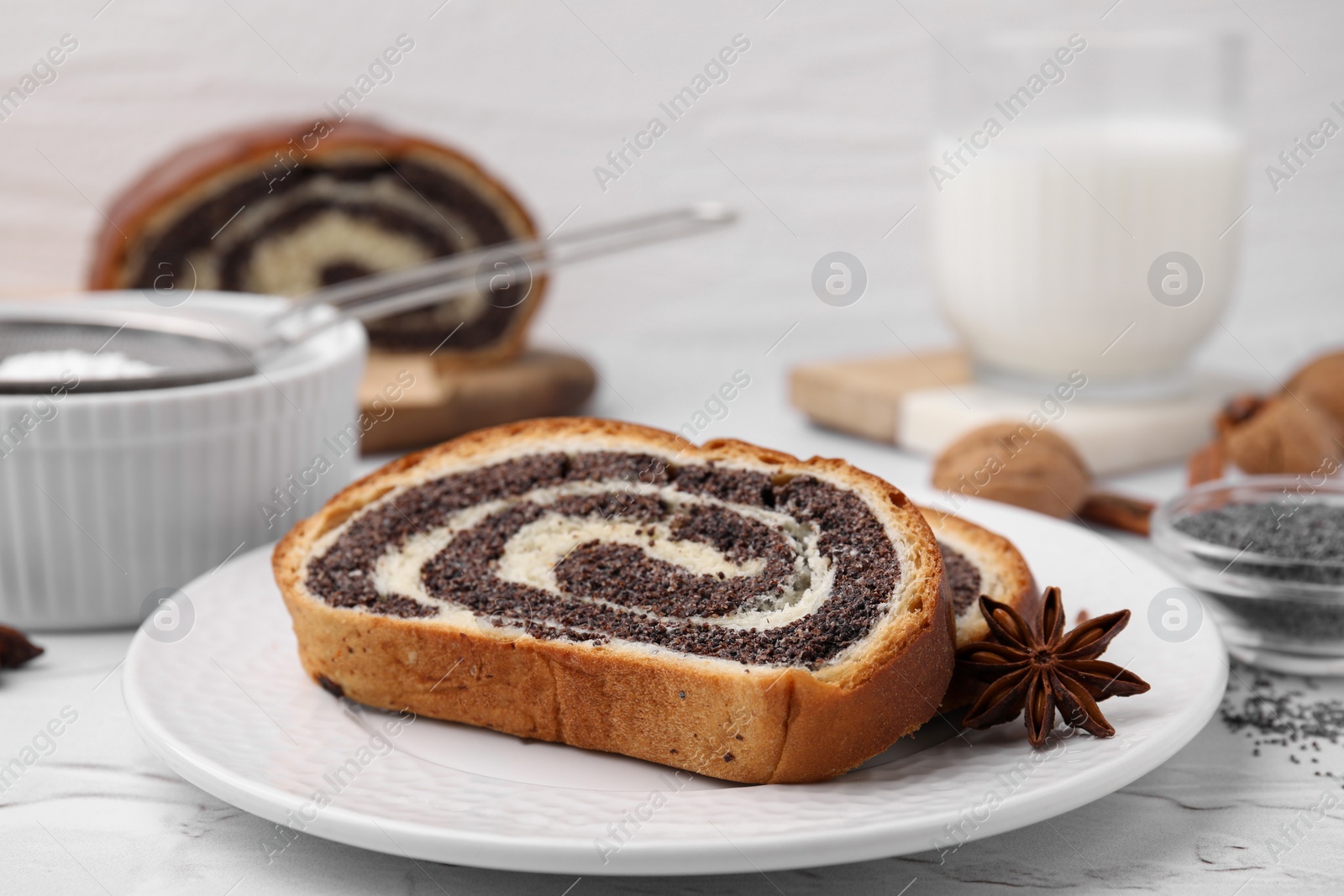 Photo of Slices of poppy seed roll and anise star on white table, closeup with space for text. Tasty cake