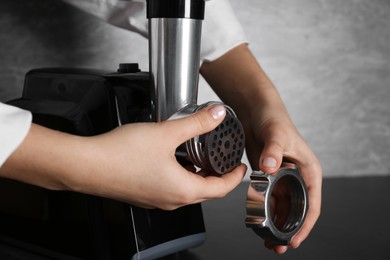 Photo of Woman assembling electric meat grinder at black table, closeup