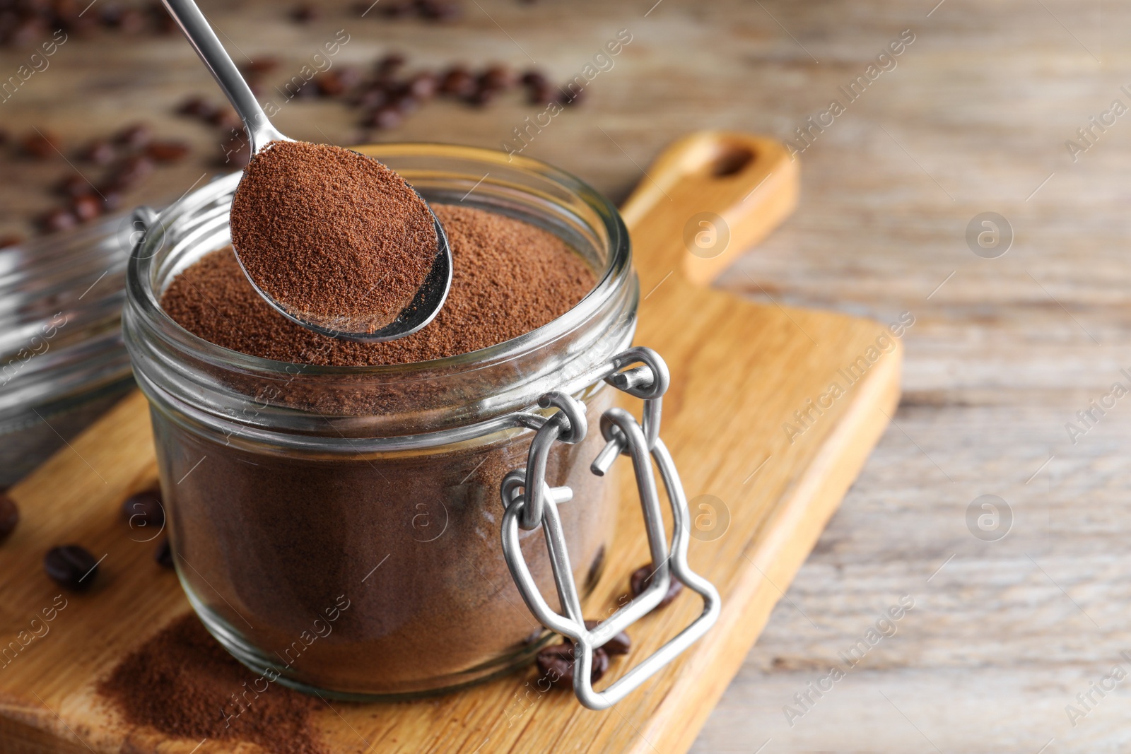 Photo of Instant coffee and spoon above glass jar on wooden table, closeup. Space for text