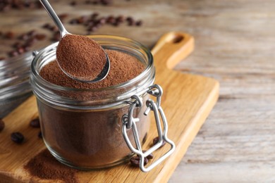 Instant coffee and spoon above glass jar on wooden table, closeup. Space for text