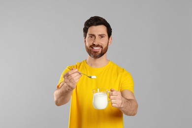 Handsome man with delicious yogurt and spoon on light grey background