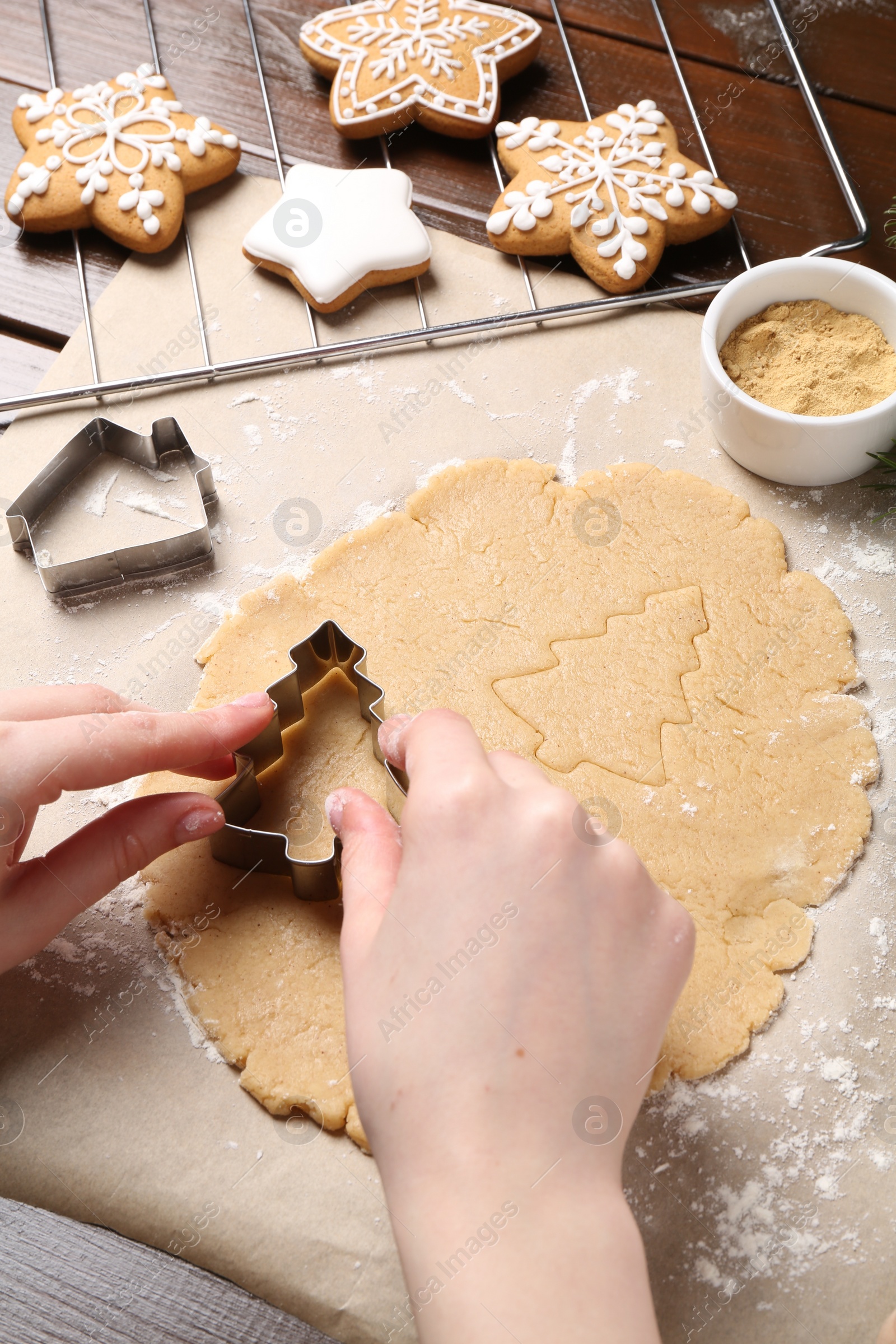 Photo of Woman making Christmas cookies with cutters at wooden table, closeup