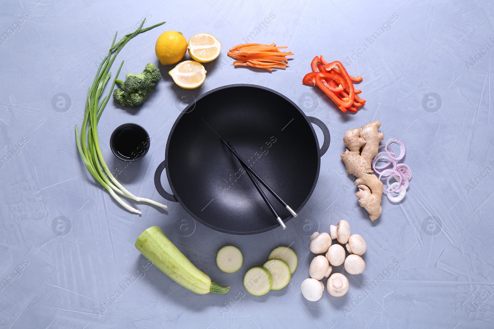 Photo of Wok, chopsticks and different products on grey table, flat lay