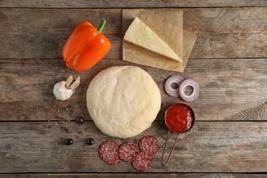 Flat lay composition with dough and ingredients for pizza on wooden table