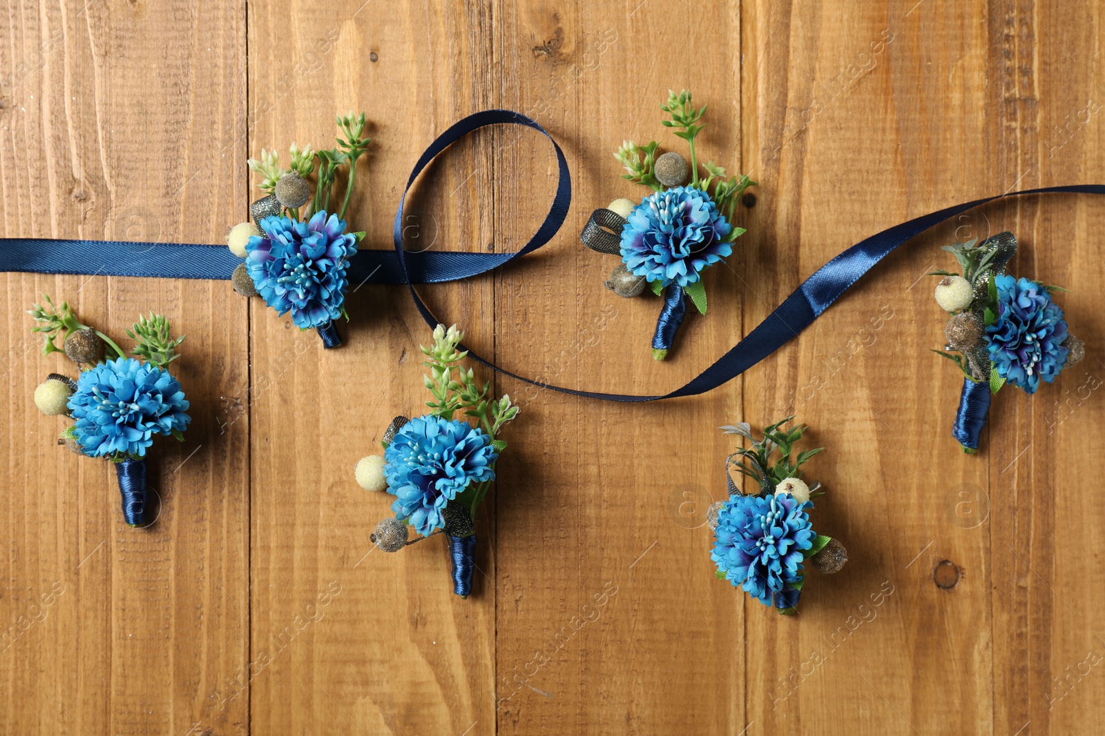 Photo of Stylish blue boutonnieres and ribbon on wooden table, flat lay
